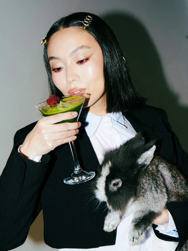 A model in black tailoring holding a matcha cocktail and a rabbit